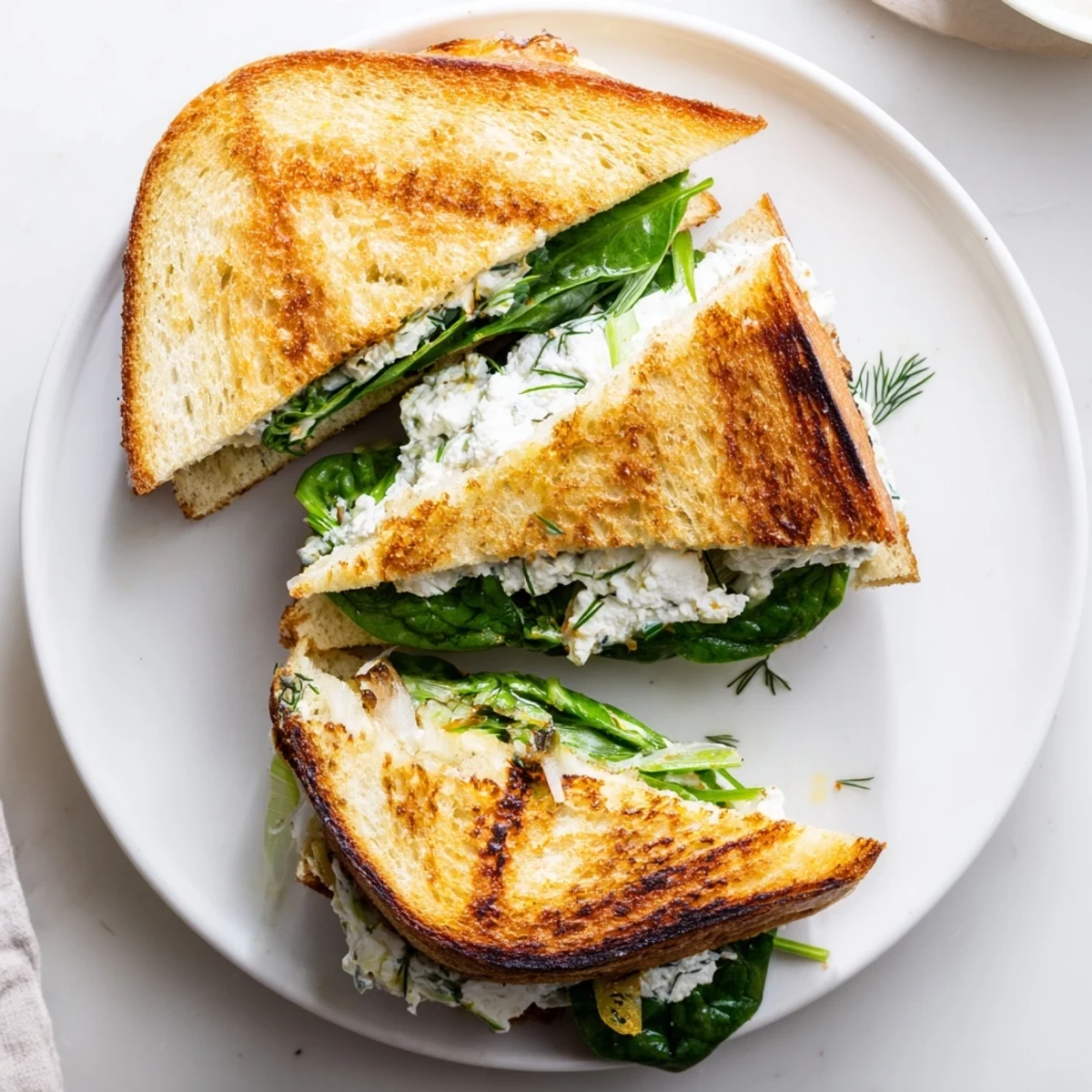 Two crispy grilled cheese halves, filled with creamy whipped feta and fresh herbs, served on a rustic plate.