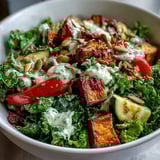 Vibrant Kale Salad Bowl with golden roasted sweet potatoes, red peppers, and zucchini in a creamy tahini dressing.
