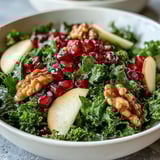 Colorful Kale and Pomegranate Bowl arranged in a ceramic bowl, featuring crisp apple slices and chopped walnuts over tender kale, glistening with a honey-Dijon dressing.