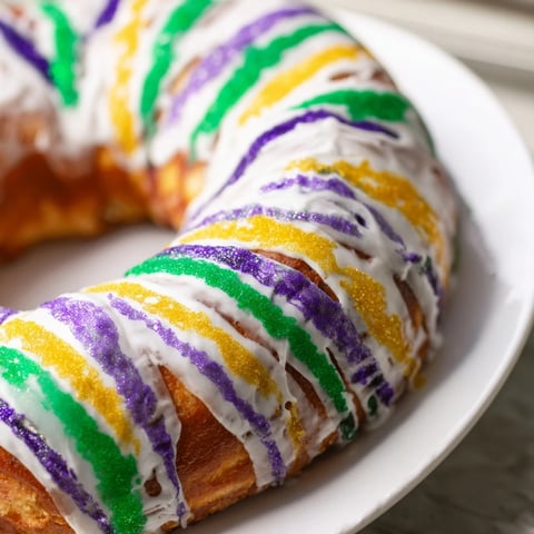 Golden, ring-shaped King Cake, drizzled with colorful icing, ready for Mardi Gras celebrations.