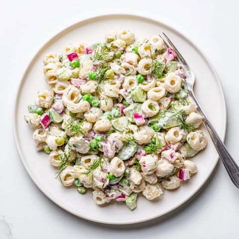 A vibrant bowl of Creamy Dill Pickle Pasta Salad with ditalini, peas, and chopped dill pickles, glistening with zesty dressing.