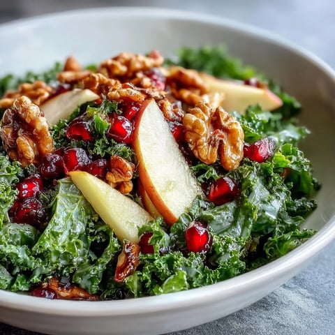 Freshly massaged kale topped with sliced apple, ruby-red pomegranate seeds, and crunchy walnuts, all tossed in a tangy apple cider vinaigrette. Kale and Pomegranate Bowl ready to serve.