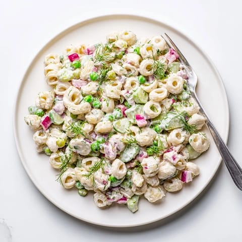 A vibrant bowl of Creamy Dill Pickle Pasta Salad with ditalini, peas, and chopped dill pickles, glistening with zesty dressing.