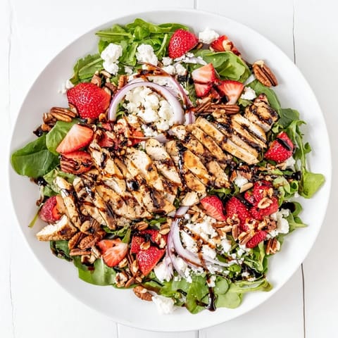 Sliced grilled chicken and fresh strawberries on mixed greens with feta, ready for the balsamic glaze drizzle.