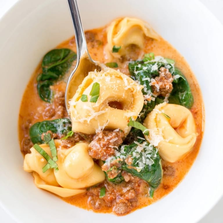 Hearty Tuscan Tortellini Soup in a white bowl, steam rising from the rich, creamy broth with Italian herbs.