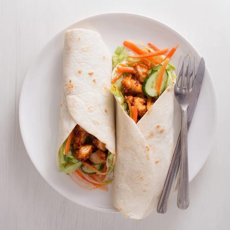 A close-up of the Honey Chili Crunch Chicken Wrap garnished with scallions, highlighting the sticky honey-chili glaze on the pan-seared chicken.