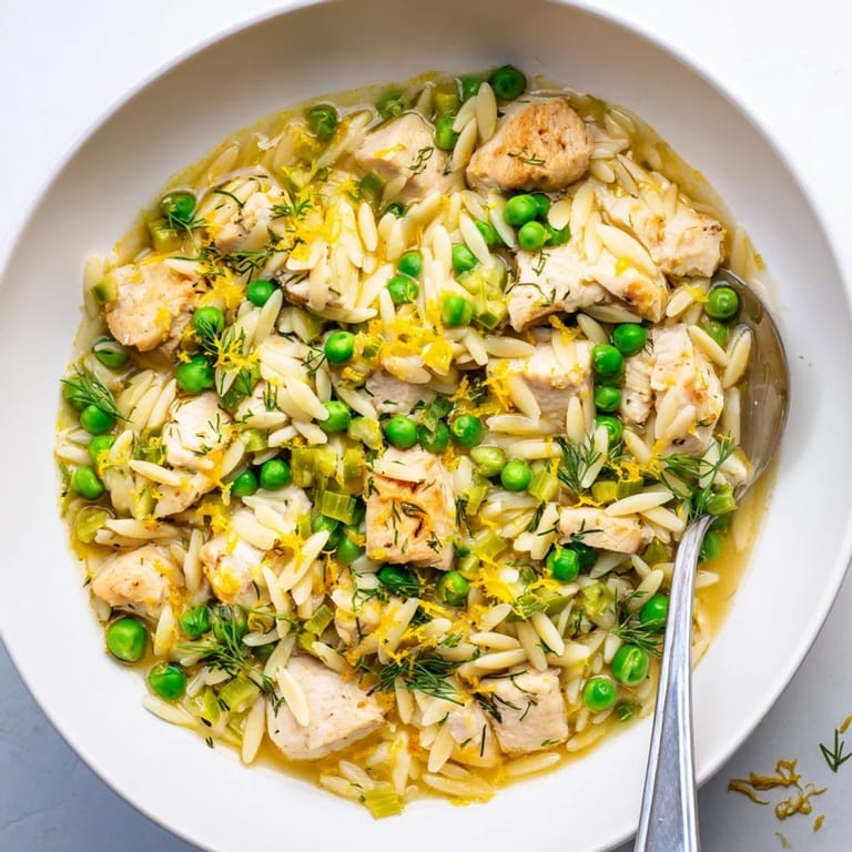 A close-up of the Lemon Herb Chicken Orzo Skillet shows glistening lemon sauce, herbs, and steaming comfort on a wooden table.