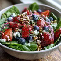 Fresh baby spinach and mixed berries tossed with creamy goat cheese and toasted walnuts in a vibrant salad bowl.