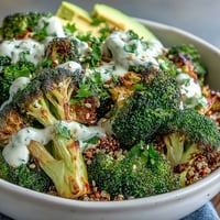 Golden roasted broccoli and red onion over fluffy quinoa, drizzled with creamy tahini sauce in a bowl.